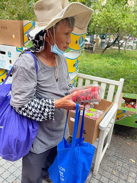 Older woman standing near distribution benches holding fresh strawberries